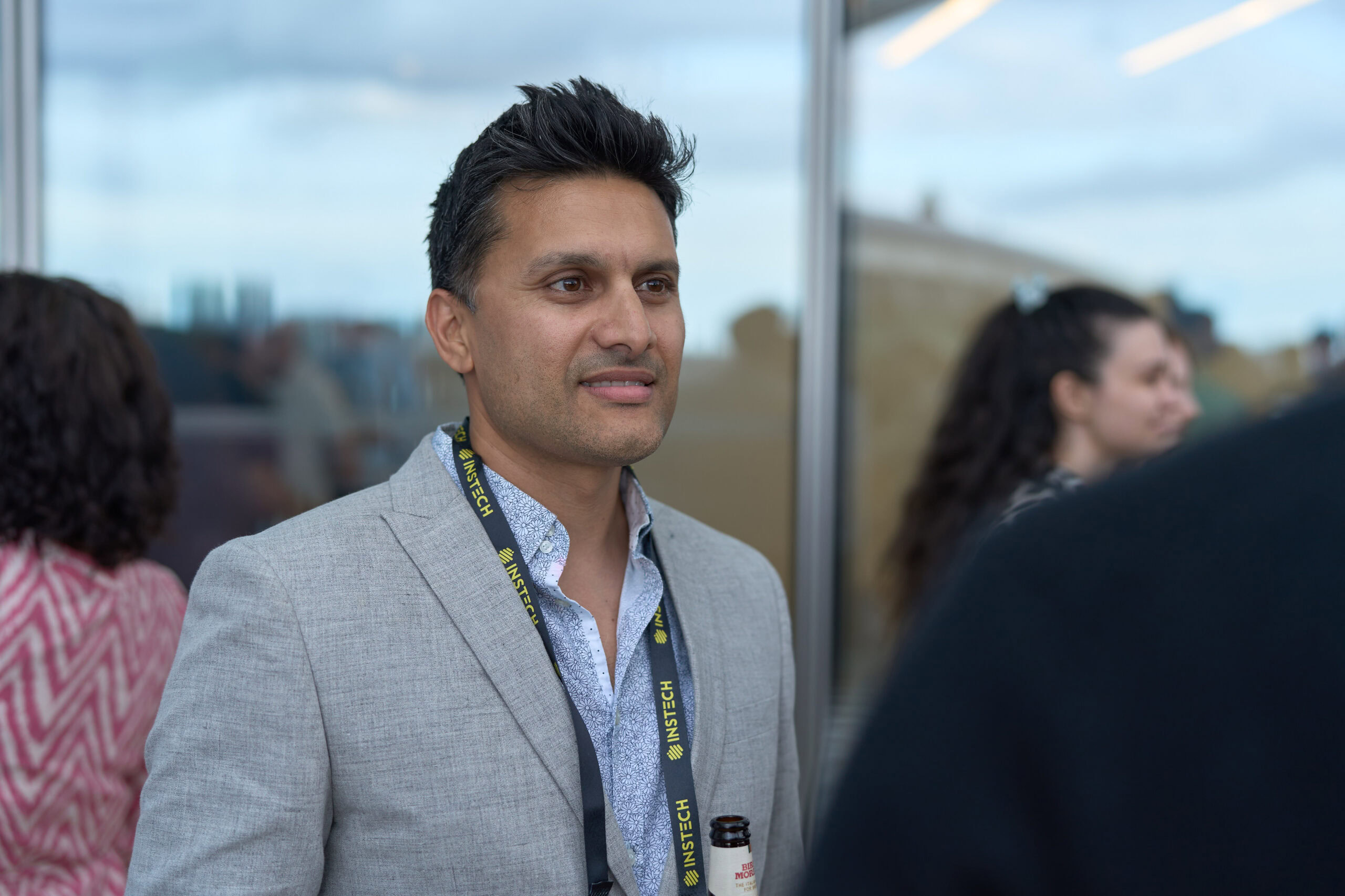 Corporate event photography by Adam Toth at Tadam Photography, featuring a professional male in a light grey suit at a networking event in London. Captured with natural lighting, the subject exudes confidence with a relaxed pose and engaging expression. The setting in Canary Wharf is blurred in the background, highlighting a modern, dynamic atmosphere.