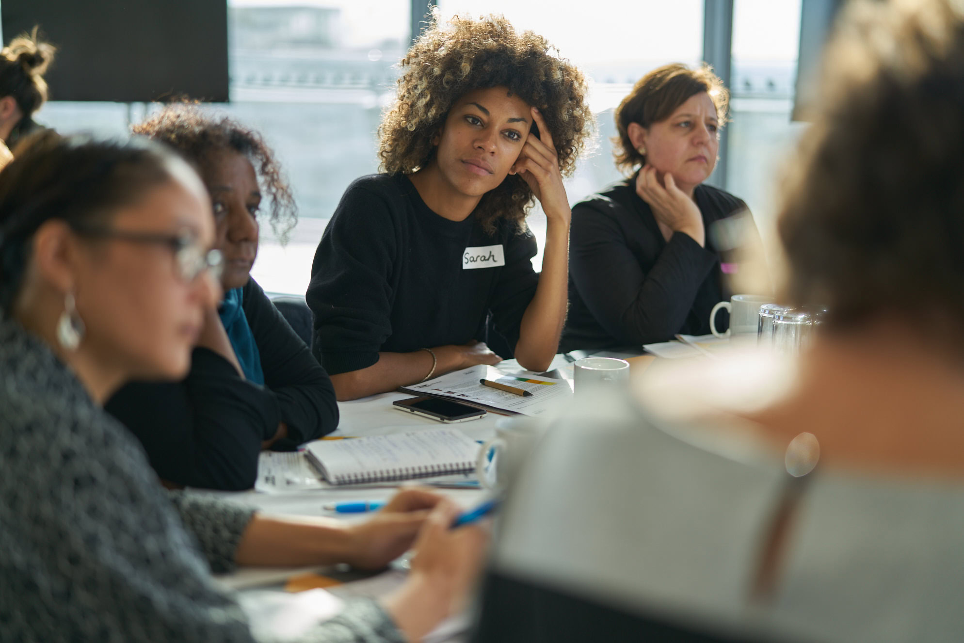 A group of individuals participating in a meeting, with one woman in focus looking thoughtful.