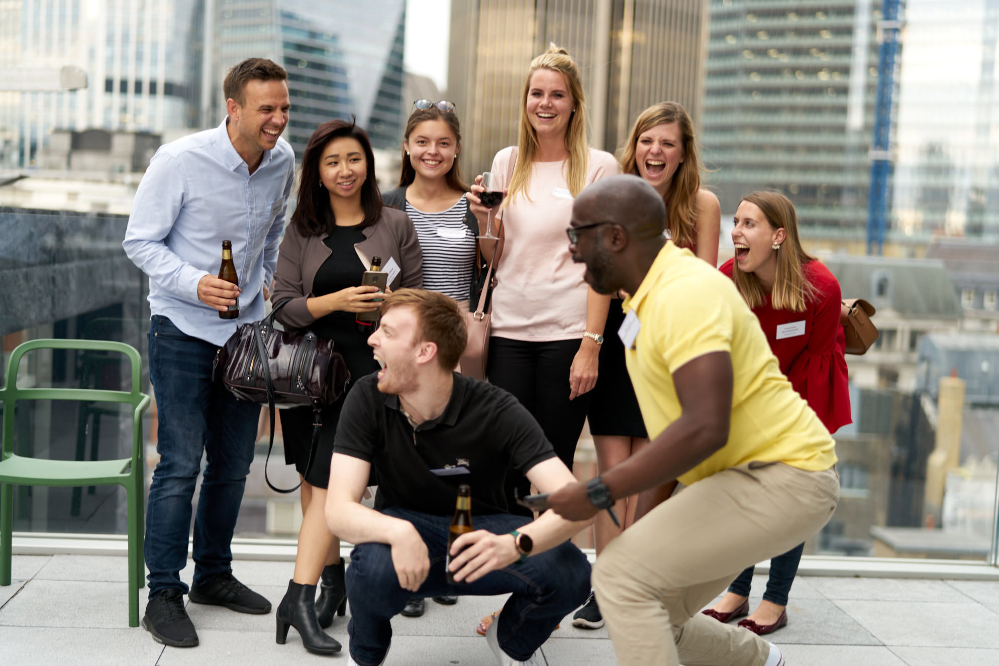 A group of nine people posing together outdoors, some holding drinks and smiling at the camera.