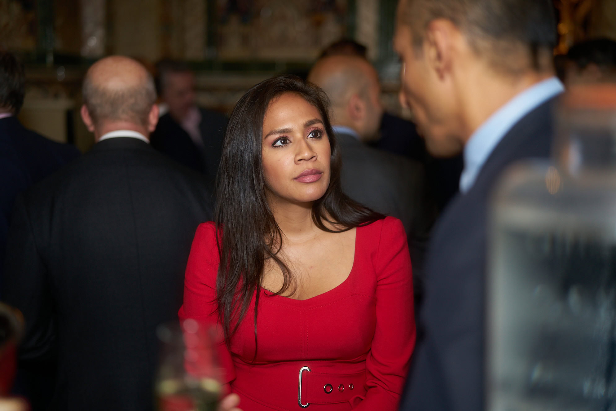 Woman wearing a red dress with a belt, engaged in conversation at a social event.