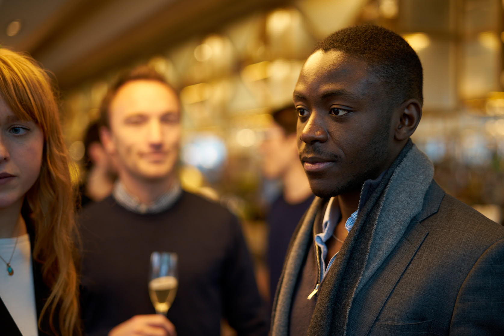 A man in a suit with a grey scarf and a woman with red hair at a social gathering.