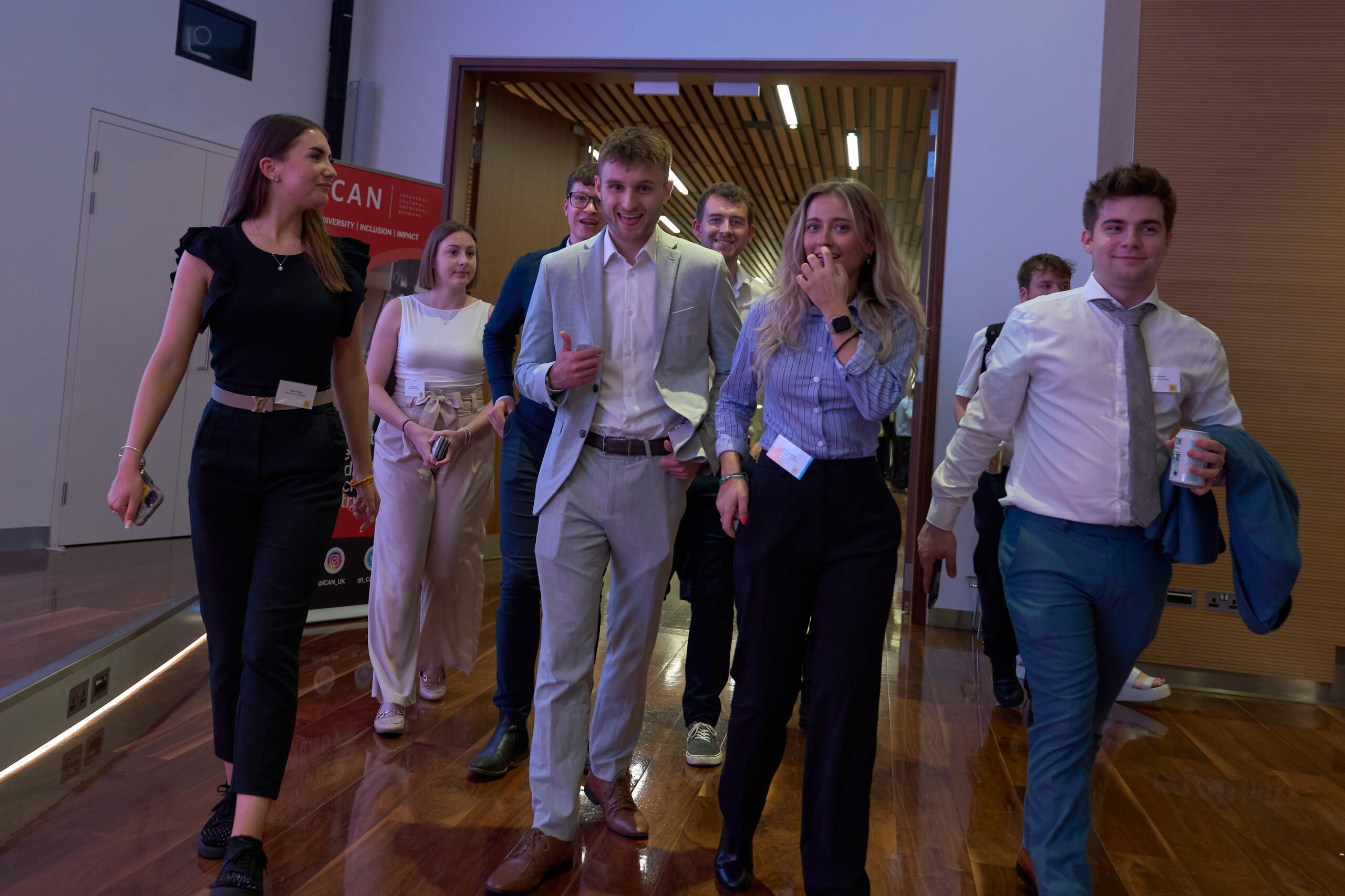 A group of young professionals walking together in a conference hall, dressed in formal attire.