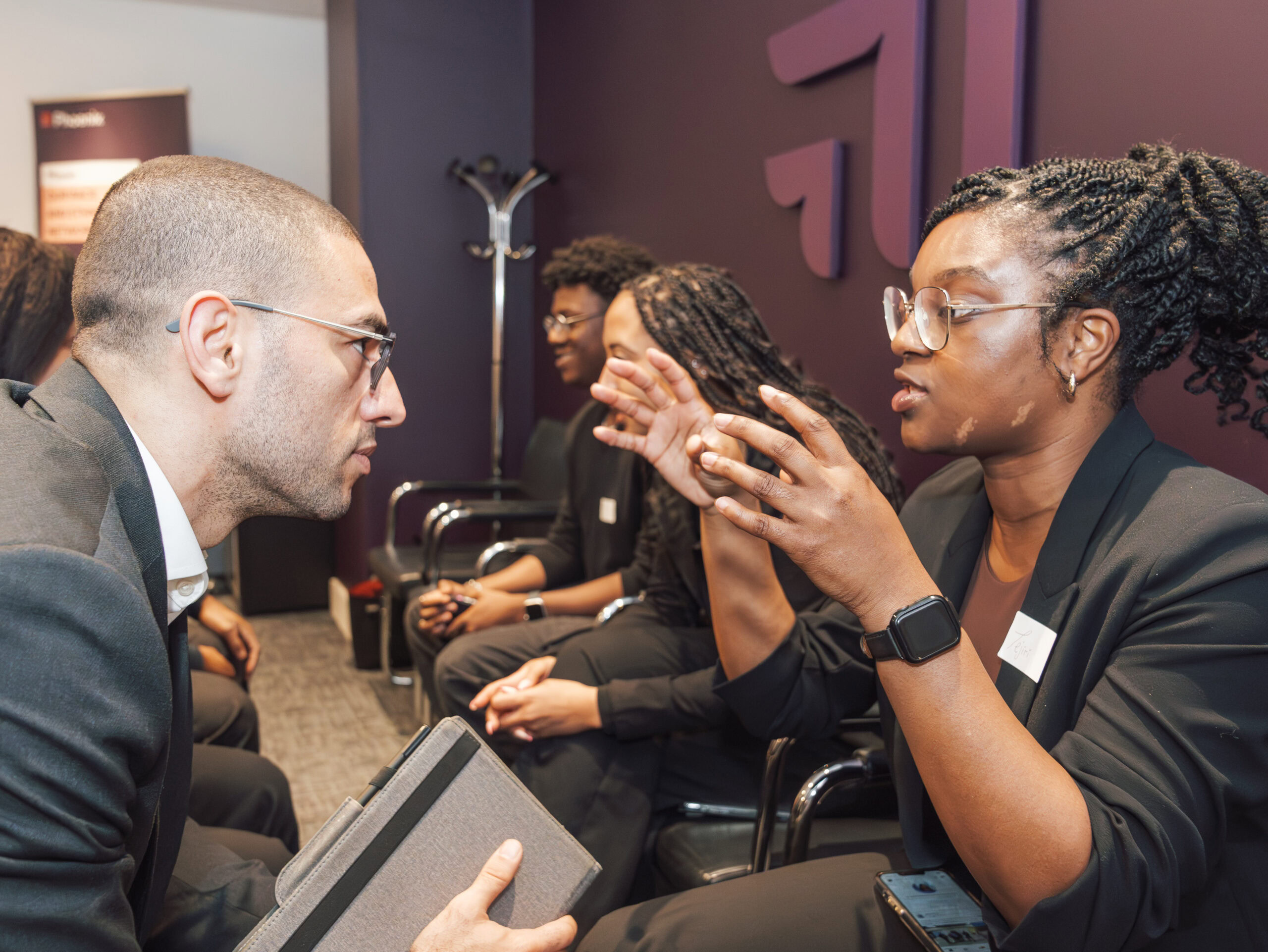 Two professionals engaged in a discussion during a group meeting in business attire.