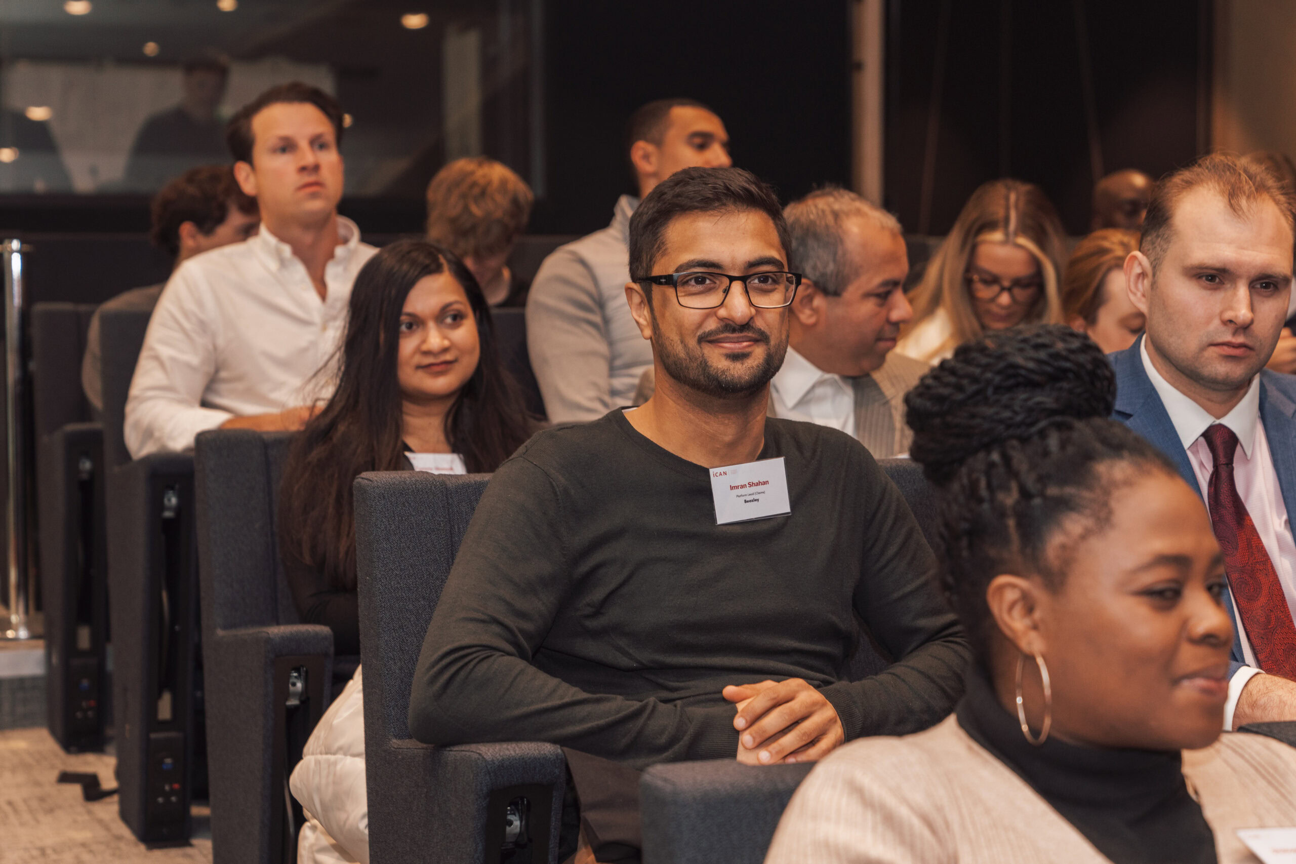 A diverse group of attendees seated in a conference room, some looking towards the front.