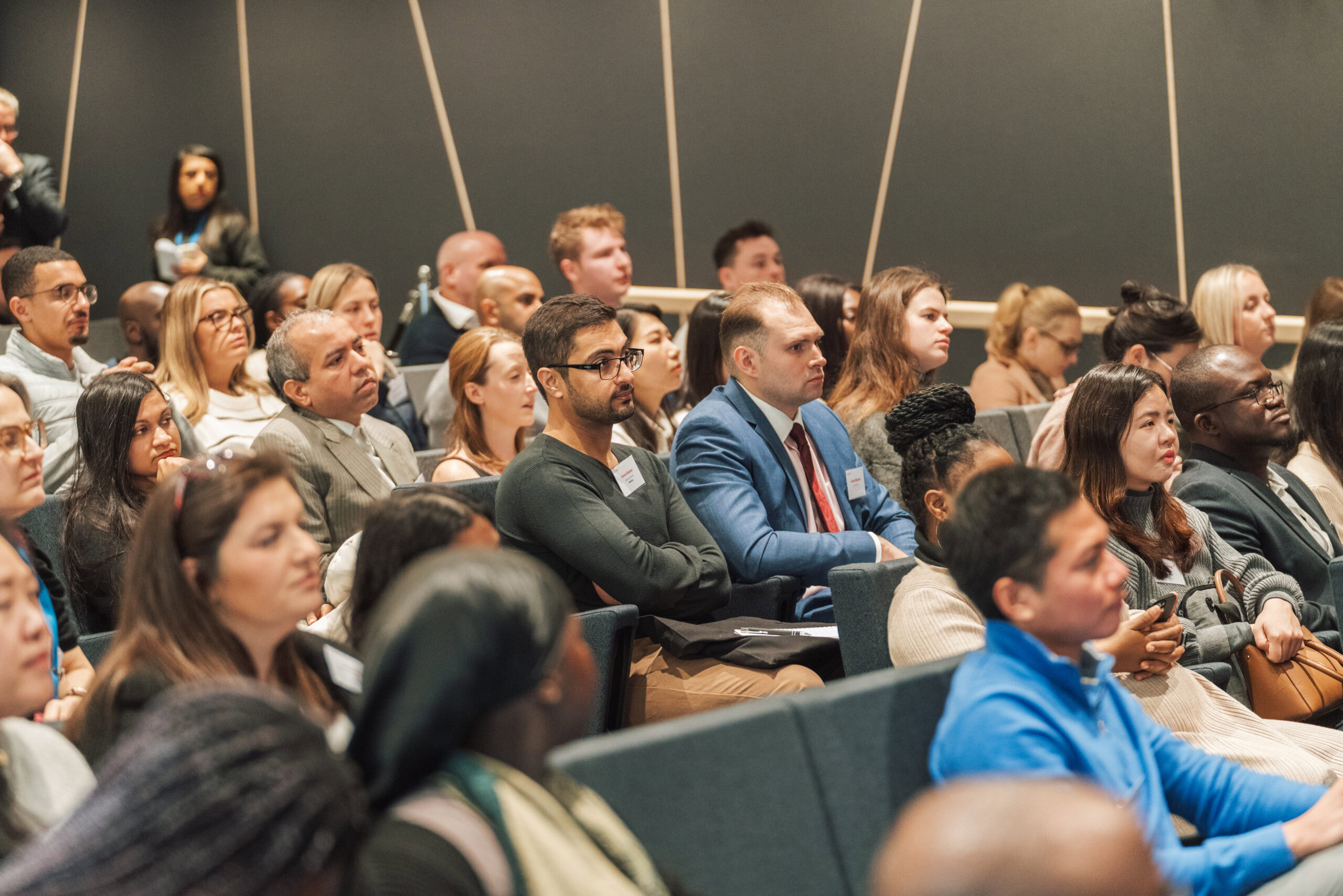 A diverse audience seated in a conference room, attentively listening to a speaker during an event.
