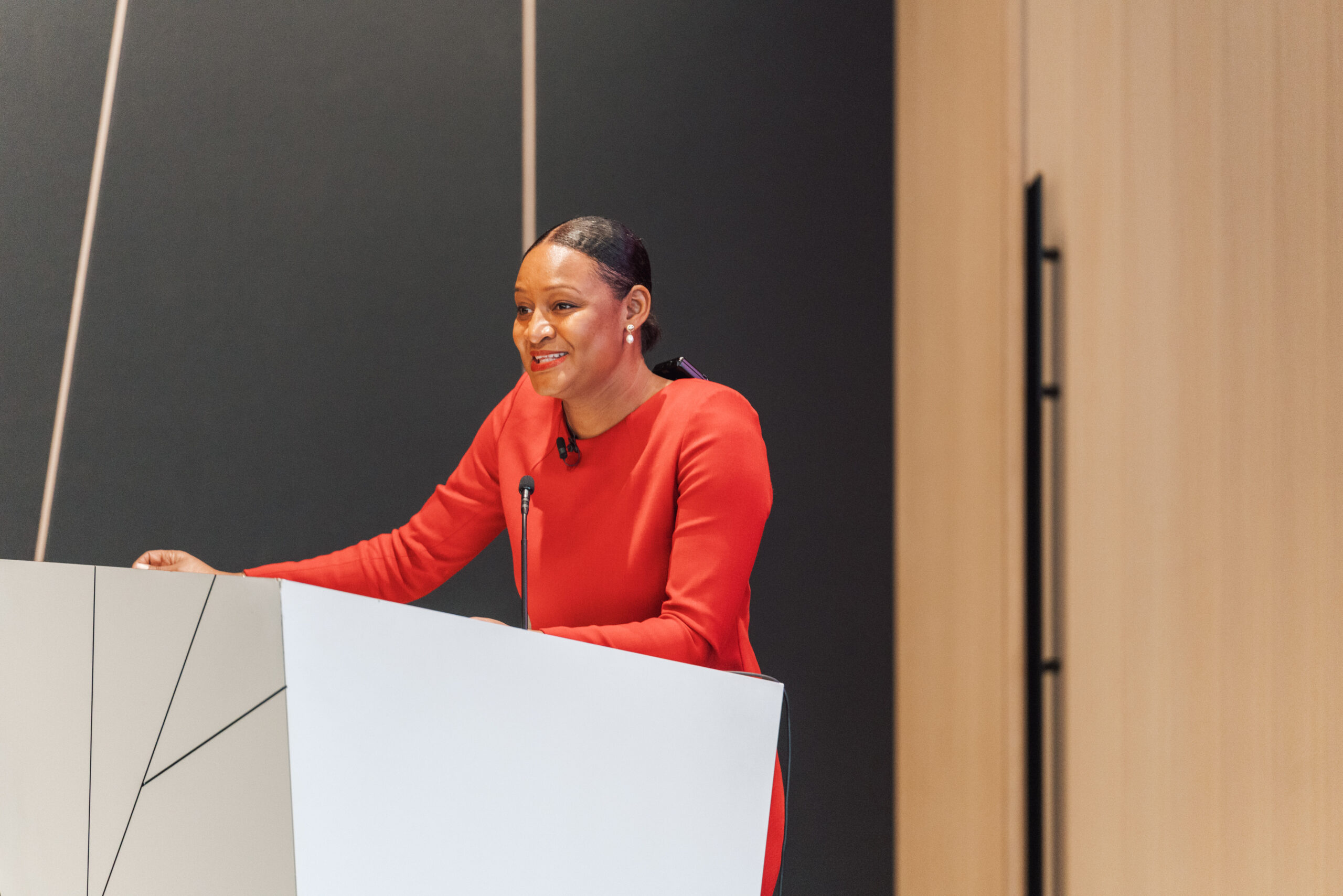 A woman wearing a red dress standing at a podium while speaking during an event.