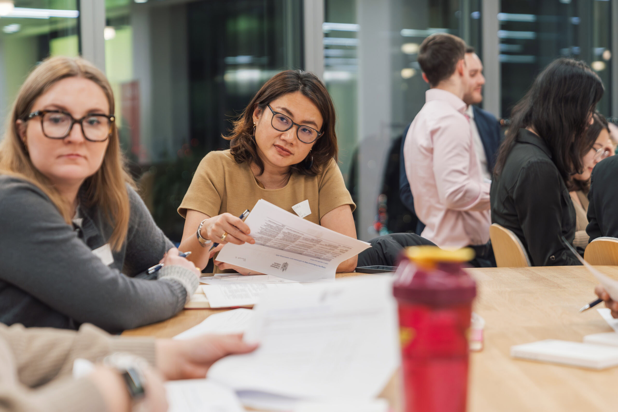 Participants engaged in a group discussion around a meeting table with documents in hand.