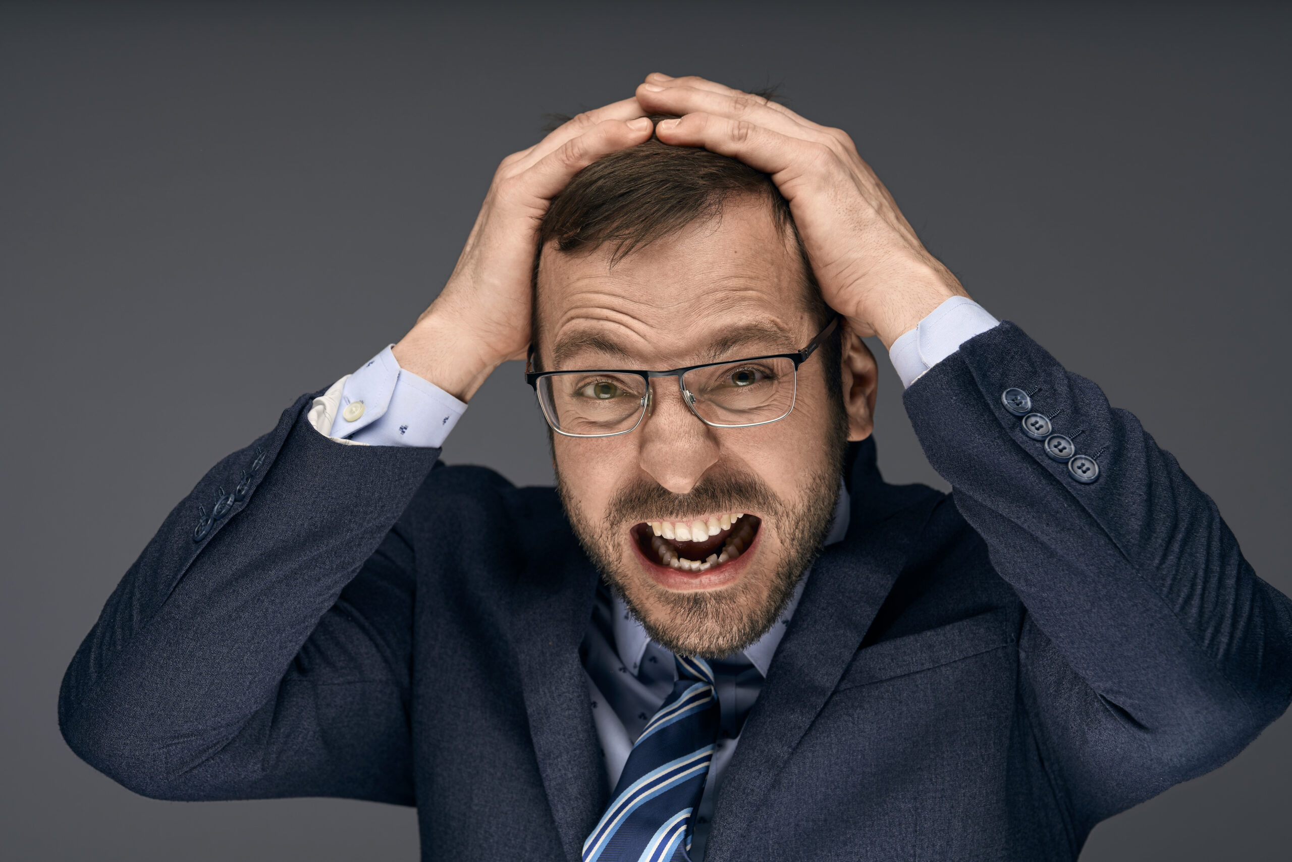 Corporate headshot of a man in a blue suit and glasses, captured in a dynamic, expressive pose. Professional studio lighting highlights his animated expression against a clean, neutral background. Photographed by Adam Toth of Tadam Photography, specializing in vibrant and authentic portraits in London, including East London and Canary Wharf.