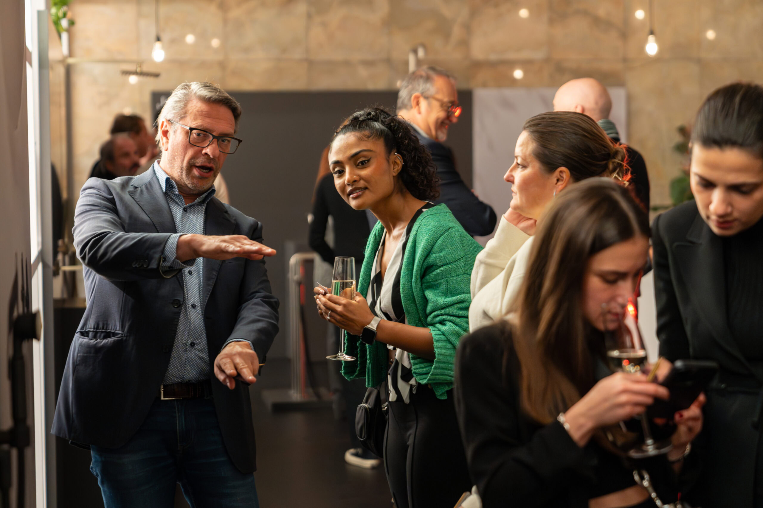 People engaged in conversation and drinking at a warmly lit social gathering.