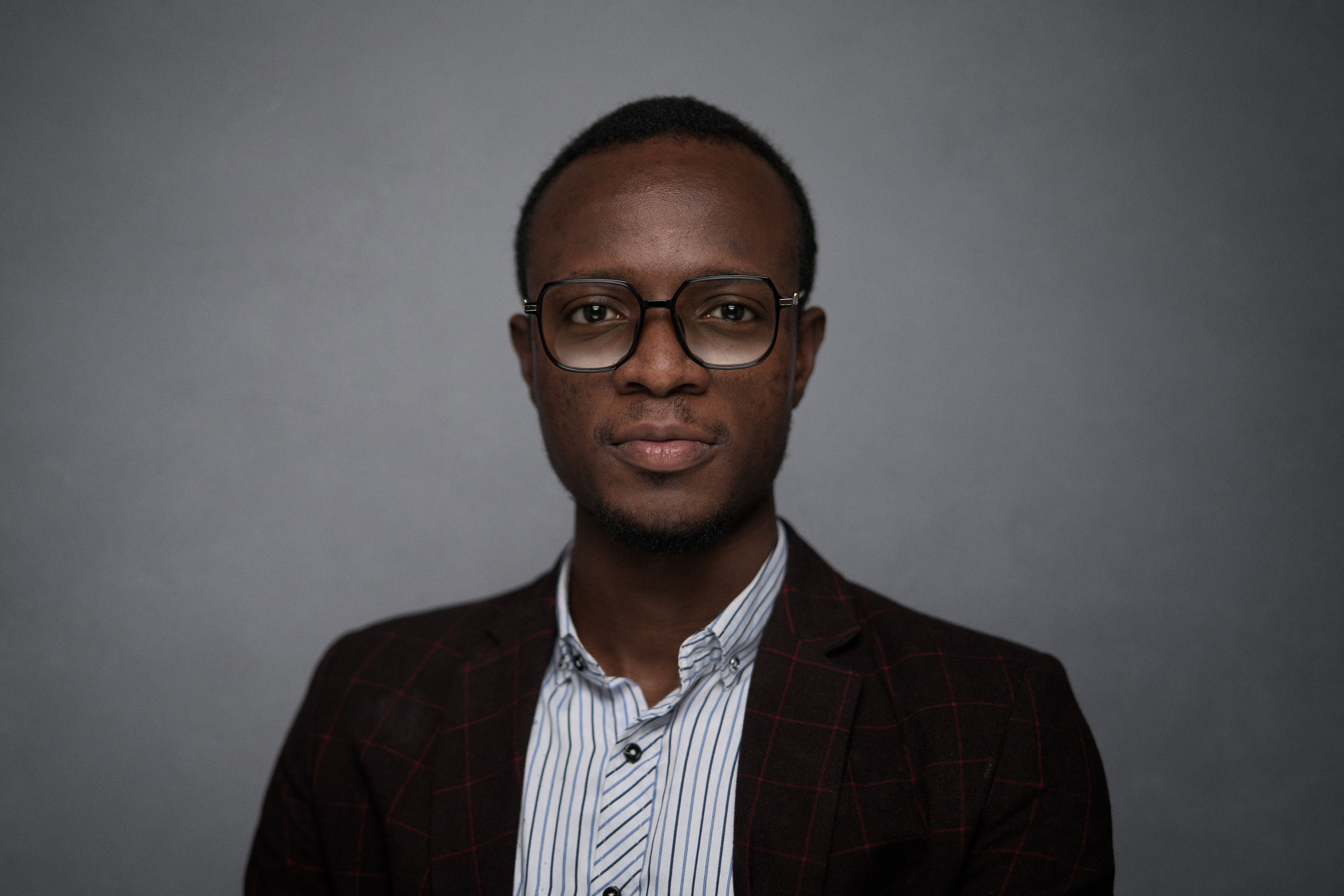 Corporate headshot captured by Adam Toth of Tadam Photography in London. The image features a poised professional with glasses, dressed in a stylish striped shirt and checkered blazer. He exhibits a confident expression against a clean, neutral backdrop, enhanced by professional studio lighting. This portrait reflects the modern and approachable style characteristic of Toth's work, perfect for