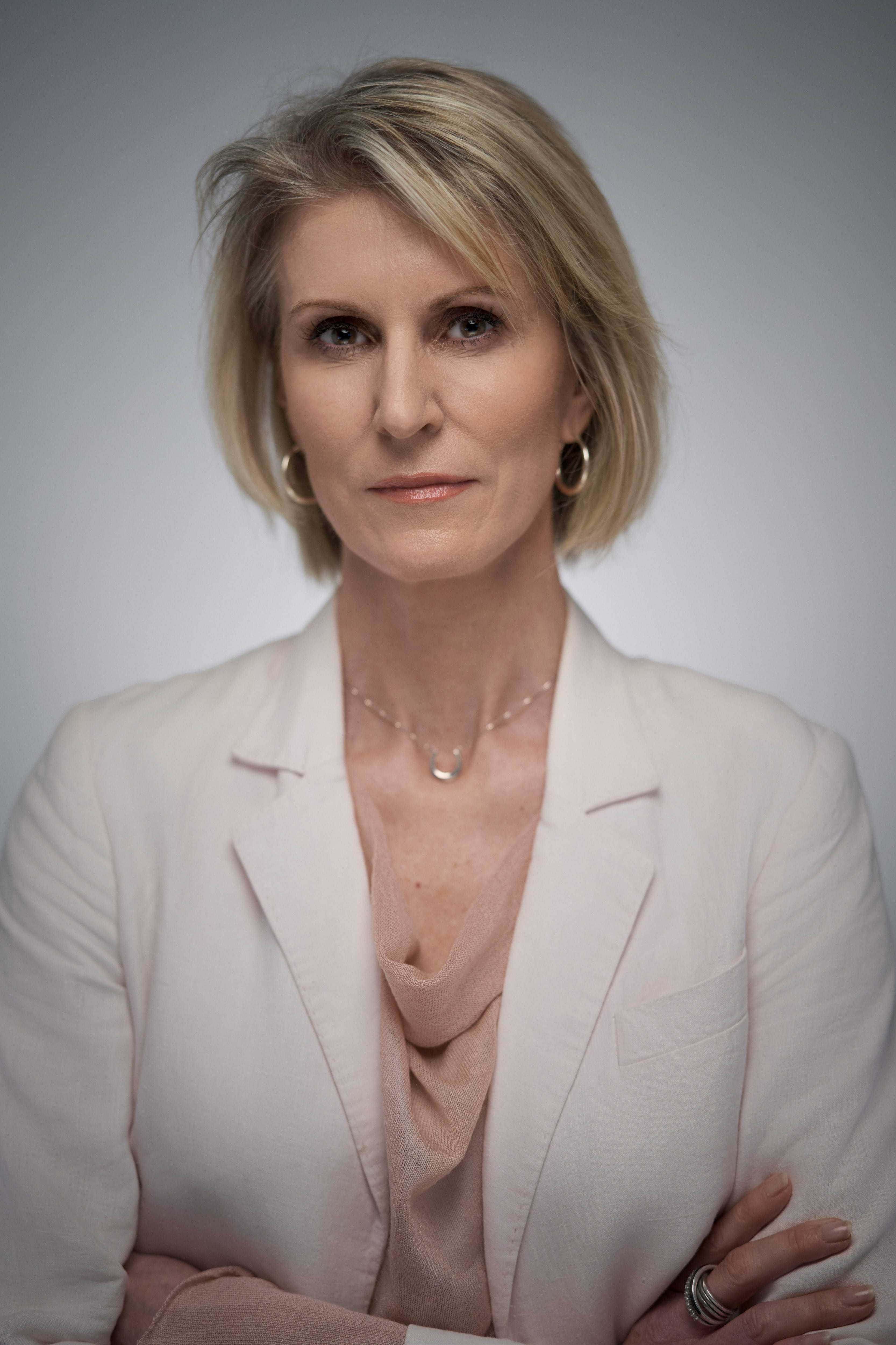 Corporate headshot of a confident woman with short blonde hair, wearing a pastel blazer and subtle jewelry, captured in a natural pose. The image features professional studio lighting with a clean background, highlighting her poised expression. Shot by Adam Toth of Tadam Photography, this image embodies professionalism and elegance, situated in London.
