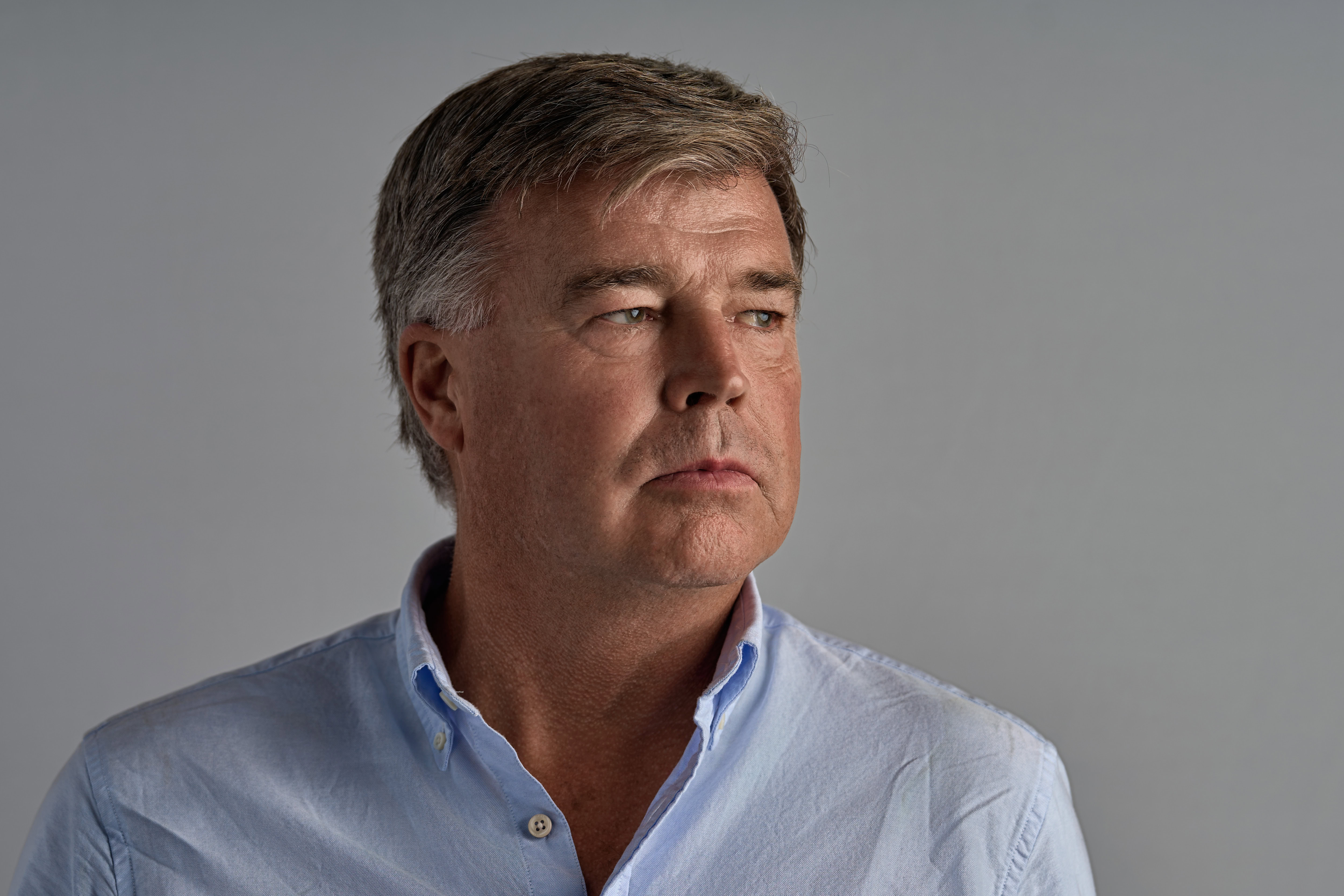 This corporate headshot, captured by Adam Toth of Tadam Photography, features a confident professional in a light blue shirt gazing thoughtfully to the side. The subject's natural pose is enhanced by clean, even lighting against a minimalist background, creating an authentic and approachable impression. This image, taken in London, exemplifies the refined style and expertise of