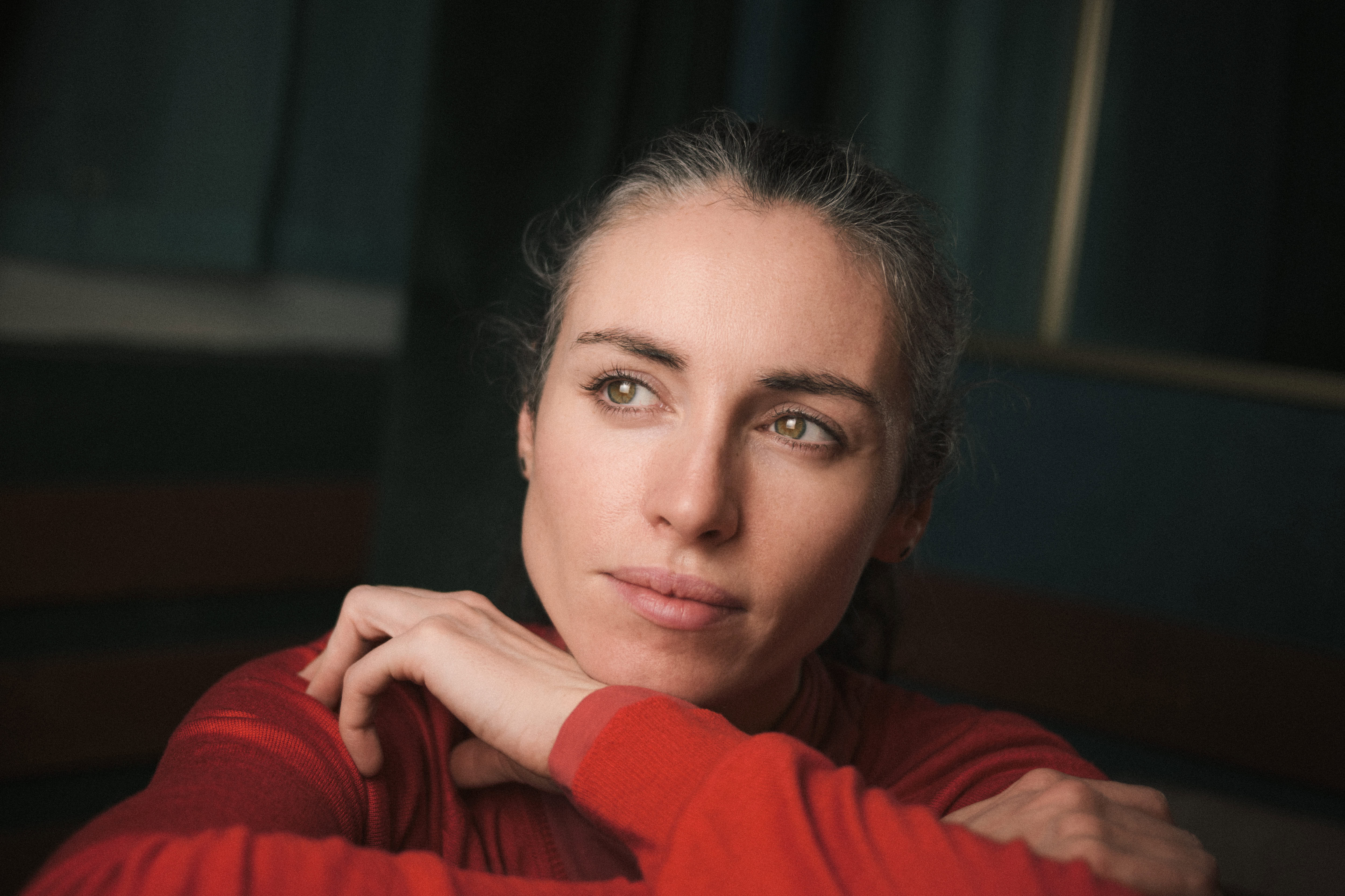Portrait of a woman captured by Adam Toth at Tadam Photography. The woman gazes thoughtfully into the distance, her arms gently crossed. The soft lighting creates a serene, intimate mood, complemented by the dark, moody background. Taken in London, this photograph exemplifies Toth's expertise in creating compelling and authentic portraits.