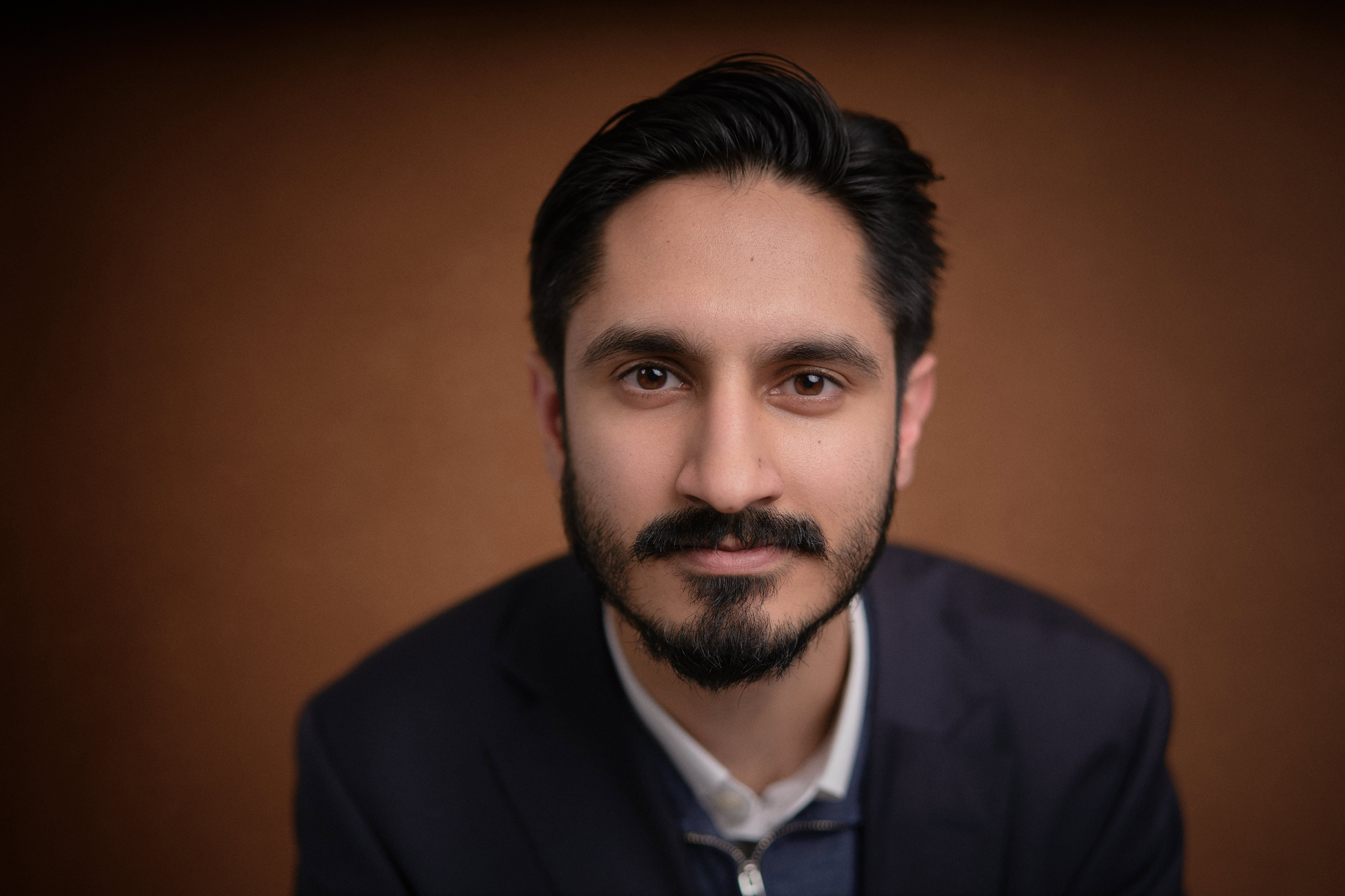 Corporate headshot captured by Adam Toth at Tadam Photography, featuring a confident professional in a dark blazer and light-colored shirt, exuding a poised and approachable demeanor. The subject's natural expression is enhanced by professional studio lighting, set against a warm, clean background. This photograph exemplifies modern corporate photography and was taken in East London, conveying a