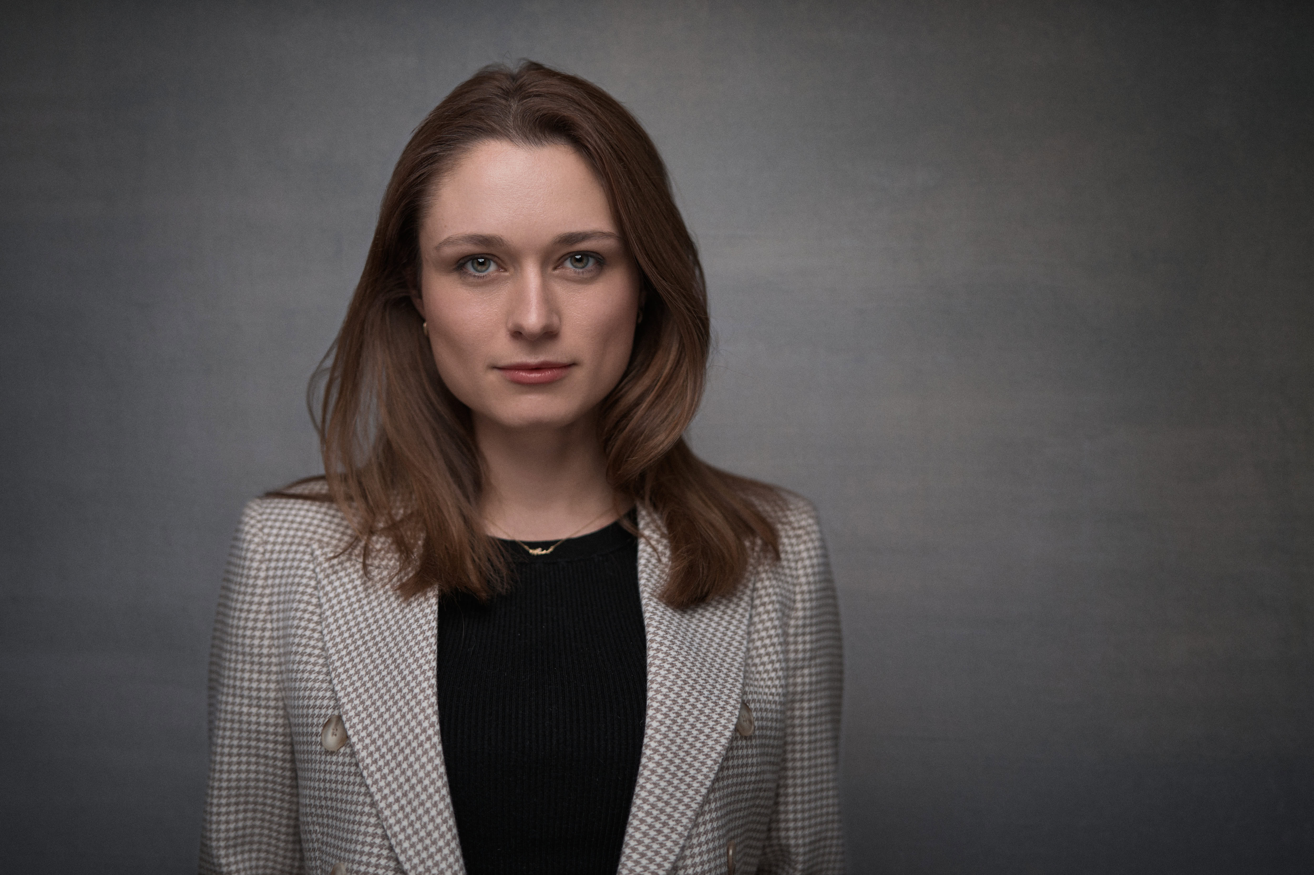 Corporate headshot captured by Adam Toth of Tadam Photography in London. The image features a confident professional woman in a chic, checker-patterned blazer, set against a clean, subdued background. The subject poses naturally, exuding a poised and approachable demeanor. Professional studio lighting highlights her features, creating a crisp and engaging portrait. Ideal for business or