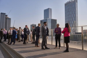 People in business attire socializing on a rooftop terrace with city skyscrapers in the background