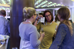 Three individuals at a networking event, two holding drinks and one displaying a name tag.