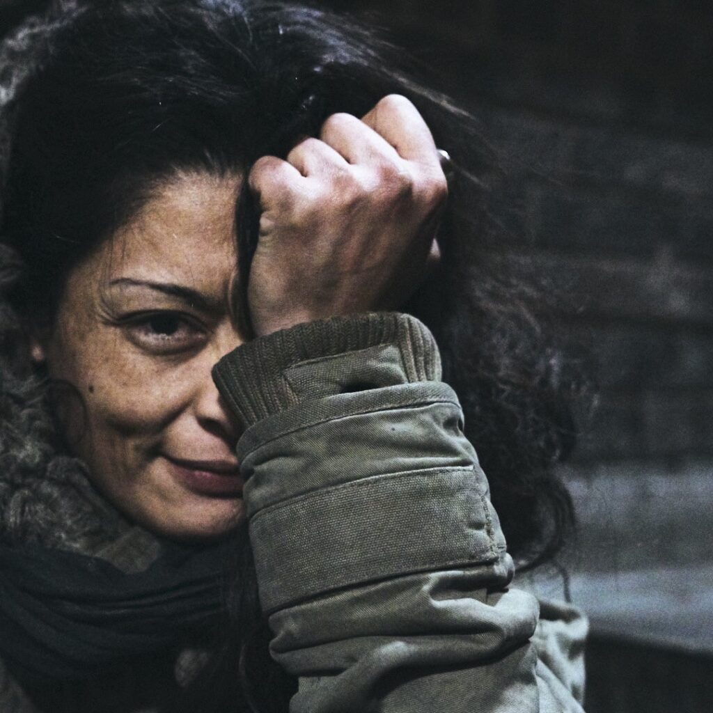 ```markdown Portrait of a woman in casual winter attire with a thoughtful expression, capturing an intimate moment in a moody outdoor setting. The subject is framed off-center, enhancing the emotional depth of the image. Shot in East London with natural lighting, highlighting the textured brick background. Photographed by Adam Toth of Tadam Photography, renowned in London