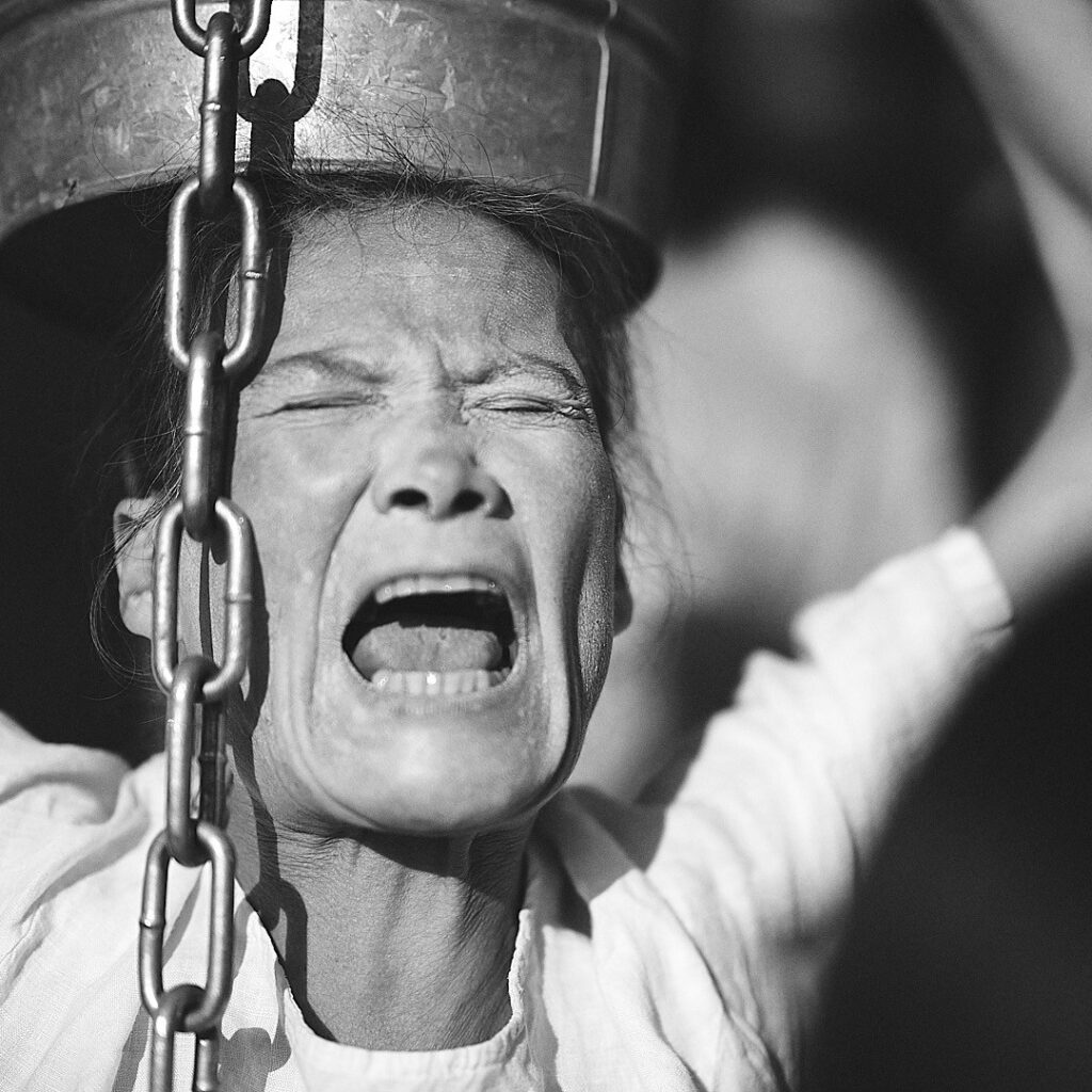 A woman with a distressed expression, holding a bucket on her head while screaming.