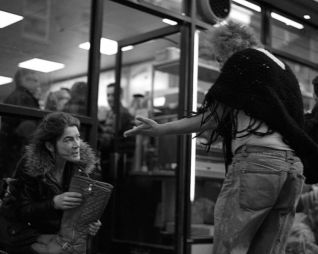 A woman seated on the floor engaging with another person in a public area.