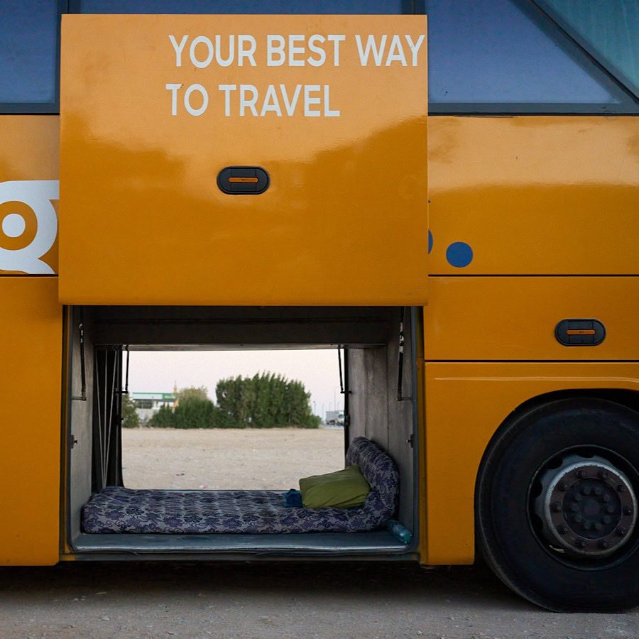Creative travel-themed photograph by Adam Toth at Tadam Photography, featuring a unique bus setup in London. The image captures a cozy, makeshift sleeping area inside an open compartment of a vibrant yellow bus, suggesting innovative travel experiences. The natural outdoor lighting and the sparse surroundings create an adventurous and intriguing mood, reinforcing Tadam Photography’s distinctive style.