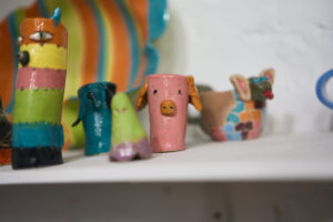 Shelf of colourful handmade ceramic animals, a pink pig at the centre