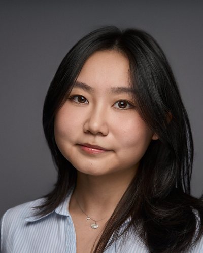Headshot of a woman with shoulder-length black hair in a pale blue shirt, soft smile on a grey backdrop